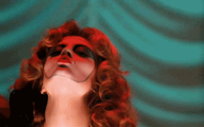 Gif of the character Janet Weiss from Rocky Horror Picture Show during the song "Rose Tint My World" near the end of the film. She has on red lipstick, teal eyeshadow, and a white painted face outlined in teal. She is moving her head downwards